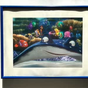 May include: A framed print of a cartoon blue stingray with a big smile, surrounded by colorful fish, including a clownfish, a seahorse, and a yellow tang. The print is set against a blue background.