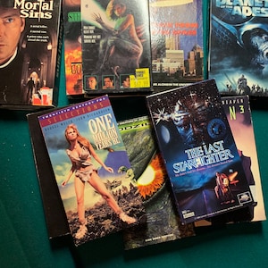 May include: A collection of VHS tapes featuring various movie titles, including "Mortal Sins", "Species", "One Million Years BC", "The Last Starfighter", and "Planet of the Apes".