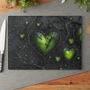 Pode incluir: Uma tábua de corte retangular com um fundo escuro texturizado com várias formas de coração verdes. Os corações têm uma aparência brilhante com detalhes de gotículas de água. A tábua é cercada por uma borda preta.