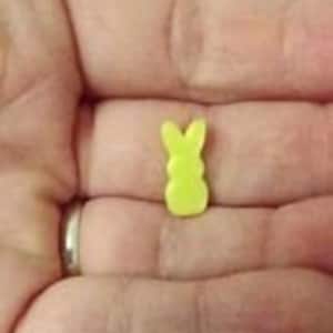 Może przedstawiać: Mały żółty króliczek Peep w kształcie królika. Cukierki są trzymane w dłoni osoby. Tekst "Tiny doll mini sized Peep bunny" jest widoczny pod cukierkami.