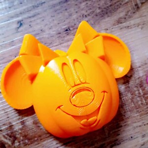 May include: Orange 3D printed Mickey Mouse head with a smiling face.