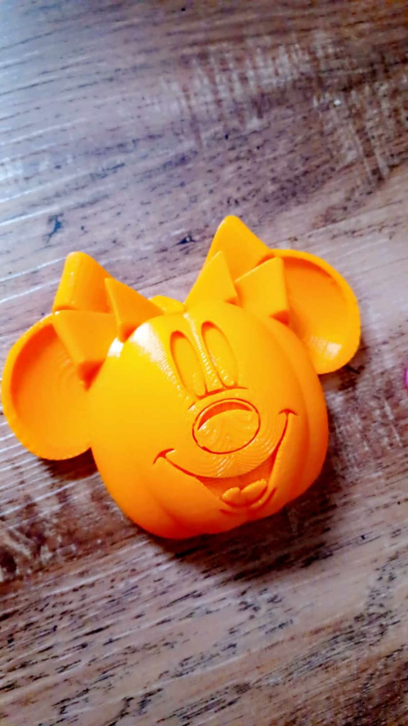 May include: Orange 3D printed Mickey Mouse head with a smiling face.
