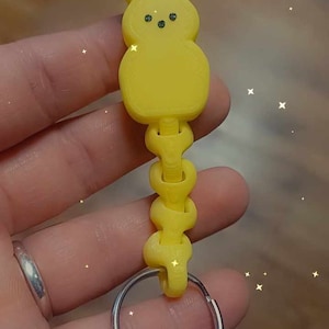 May include: A yellow 3D printed bunny keychain with a flexible link chain and a silver key ring. The text "Print-in-place Flexi Link Bunny Keyring" is printed below the keychain.