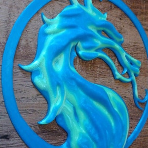 May include: A blue and green 3D printed dragon head in a circle. The dragon is facing right and has a fierce expression.