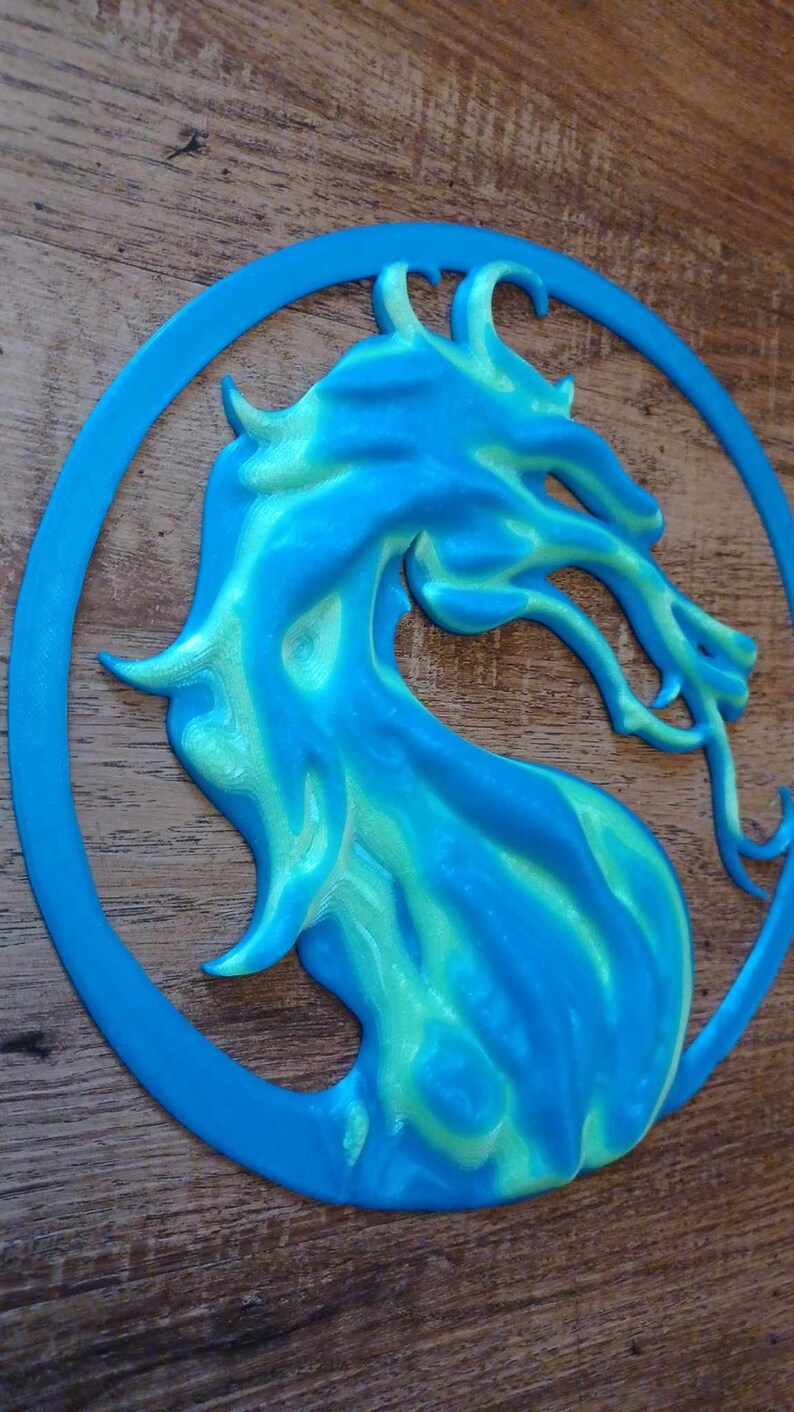 May include: A blue and green 3D printed dragon head in a circle. The dragon is facing right and has a fierce expression.