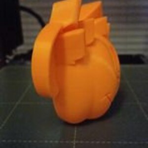 May include: Orange 3D printed model of a heart. The model is detailed and has a realistic shape.