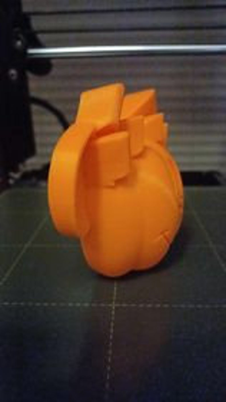 May include: Orange 3D printed model of a heart. The model is detailed and has a realistic shape.