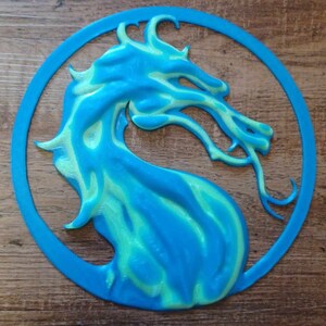 May include: A blue and green 3D printed dragon head in a circle. The dragon is facing right and has a light green and blue colour scheme.