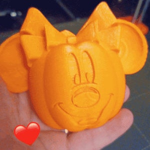 Puede incluir: Calabaza naranja impresa en 3D con una cara de Minnie Mouse tallada.