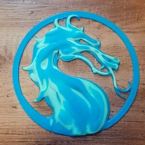 May include: A blue and green 3D printed dragon head logo. The dragon is facing the right side of the image. The logo is in a circle.