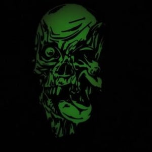 May include: A green glow-in-the-dark skull with a menacing expression. The skull is detailed with a furrowed brow, a single eye, and a wide open mouth with sharp teeth.