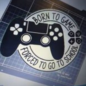 以下が含まれることがあります： ゲームコントローラーの白黒グラフィックデザインで、「Born to Game Forced to Go to School」というテキストが書かれています。