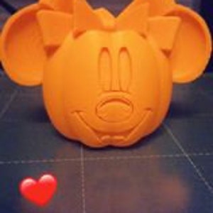 May include: An orange 3D printed pumpkin with a Minnie Mouse face and a large bow on top.