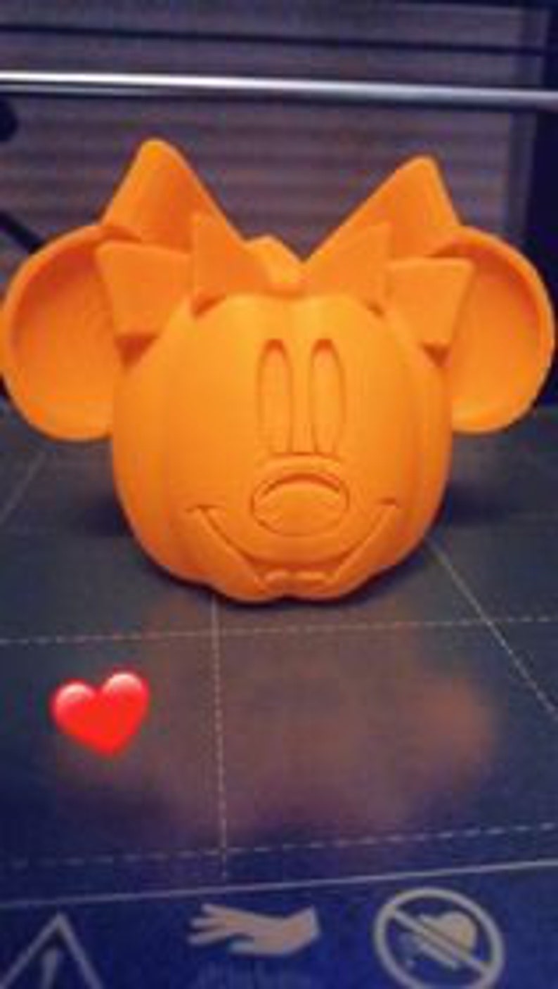 May include: An orange 3D printed pumpkin with a Minnie Mouse face and a large bow on top.