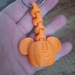 May include: Orange pumpkin-shaped keychain with Mickey Mouse ears. The keychain has a flexible chain and a silver key ring.