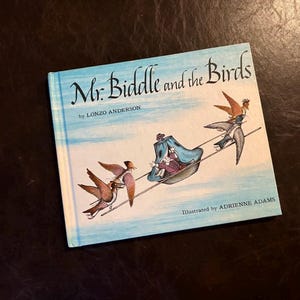 May include: A children's book titled "Mr. Biddle and the Birds" by Lonzo Anderson, illustrated by Adrienne Adams. The cover features a light blue sky background with illustrations of birds pulling a carriage.