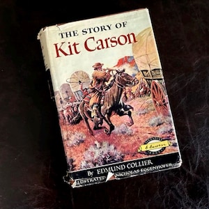 May include: Vintage hardcover book titled "The Story of Kit Carson" with a colorful illustration of a cowboy on horseback. The cover features a wagon train and desert landscape. The book is by Edmund Collier.