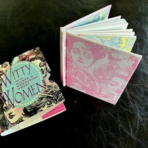 May include: Two small, pink and white hardback books. The book on the left has a black and white illustration of women on the cover and the text "Witty Women Wise, Wicked & Wonderful Words". The book on the right has a pink and white floral design on the cover.