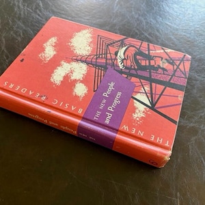 May include: A hardcover book titled The New People and Progress, part of the Basic Readers series. The cover is orange with a graphic illustration of a person climbing a black metal tower. A purple diagonal band features the title text in white.