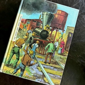 May include: A vintage book cover illustration showing a train derailment. The cover features a steam engine, a water tower, and figures of people. The title "THE ALICE AND JERRY BOOKS" is printed on the spine. The artwork is colourful and detailed.