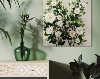 May include: Square canvas art featuring a floral design of white roses and green leaves against a beige background. The artwork is displayed on a wall, with a green glass vase and a wooden cabinet in the foreground.