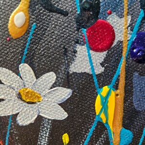 May include: Close-up of an abstract painting with a textured black background. White daisy-like flowers, yellow and red paint splatters, and turquoise lines create a vibrant, artistic composition. Gold and blue paint details add depth.