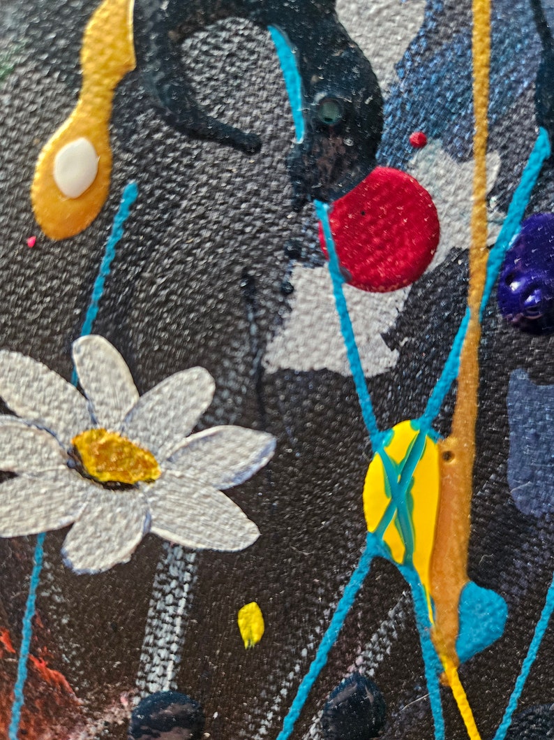 May include: Close-up of an abstract painting with a textured black background. White daisy-like flowers, yellow and red paint splatters, and turquoise lines create a vibrant, artistic composition. Gold and blue paint details add depth.