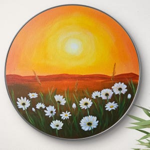 Puede incluir: Una pintura redonda que representa una puesta de sol sobre un campo de margaritas blancas. El cielo es de un naranja y amarillo vibrantes, con un sol brillante en el centro. Las margaritas están dispersas por todo el campo, con hierba verde y tallos.