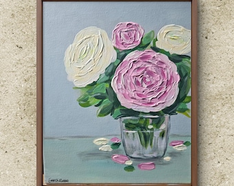 May include: A framed painting of a bouquet of white and pink flowers in a glass vase. The flowers are arranged in a loose, natural style, and the vase is clear glass. The background is a light blue color, and the painting is signed "Emma Russo" in the lower left corner.