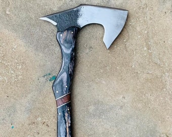 May include: A black and brown axe with a curved blade and a wooden handle. The handle is decorated with brass accents.