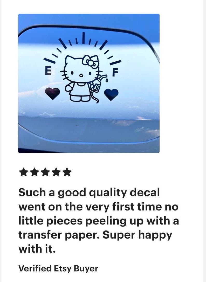 May include: A black vinyl decal applied to a smooth surface, featuring a fuel gauge graphic with the letters E and F. The design includes a cartoon cat character holding a gas pump nozzle, flanked by two solid black heart shapes on either side.
