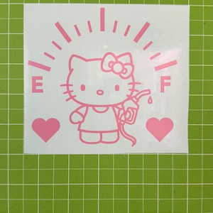 May include: A light pink vinyl decal featuring a cartoon cat character holding a gas pump nozzle. The design includes a fuel gauge arc with E and F markings, and two solid hearts on either side, all set against a white backing sheet.