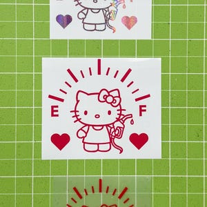 May include: Three vinyl decals featuring a Hello Kitty character holding a gas pump nozzle. Each design includes a fuel gauge arc labeled E and F, and two hearts. The top decal is holographic, while the middle and bottom decals are solid red.