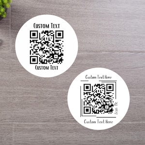 May include: Two white circular stickers with black QR codes and the text "CUSTOM TEXT" and "Custom Text Here". The stickers are on a light brown wooden surface. One sticker has the text "Scan Me".