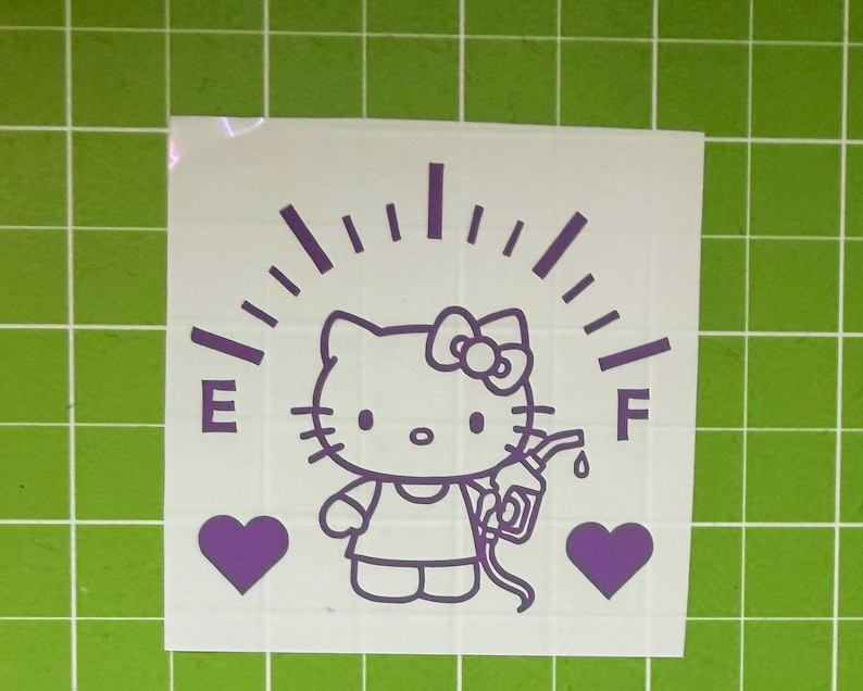 May include: A purple vinyl decal featuring a cartoon cat character with a bow, positioned below a fuel gauge arc with the letters E and F. The character holds a gas pump nozzle, flanked by two solid purple hearts on a white backing sheet.