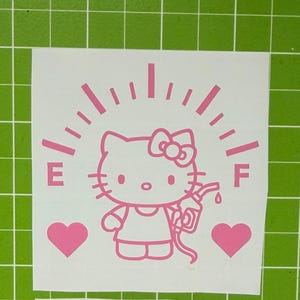 May include: A light pink vinyl decal featuring a cartoon cat character holding a fuel pump nozzle. The design includes a fuel gauge arc with the letters E and F, and two solid hearts on either side, all presented on a white backing sheet.