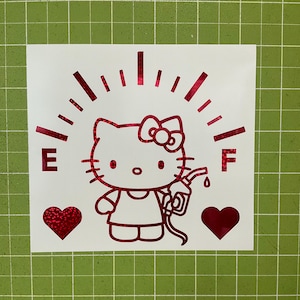 May include: A red holographic vinyl decal featuring a cartoon cat character holding a fuel pump nozzle. The design includes a fuel gauge arc with the letters E and F on either side, and two solid red hearts positioned below the character.