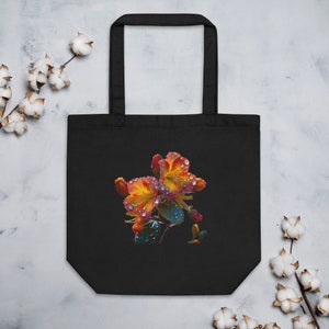 May include: Black tote bag with a colorful floral design featuring two orange and yellow flowers with water droplets on the petals. The flowers are on a green stem with leaves.