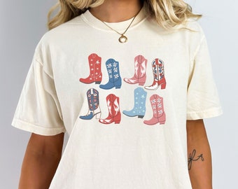 May include: A cream-colored t-shirt with a graphic of nine colorful cowboy boots with floral patterns. The boots are arranged in three rows of three.