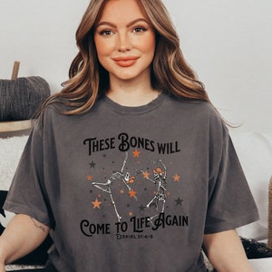 May include: A gray t-shirt with a graphic of two skeletons dancing with stars and the text "These Bones Will Come to Life Again Ezekiel 37:4-5".