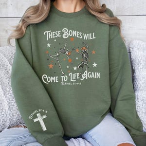 May include: Green sweatshirt with a graphic of two skeletons dancing with stars and the text "These bones will come to life again Ezekiel 37:4-5".