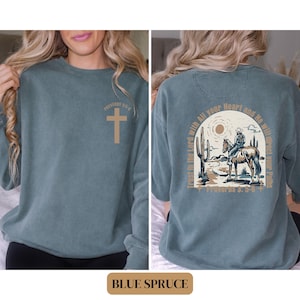 May include: A blue sweatshirt with a cross on the front and a cowboy riding a horse with the text "Trust in the Lord with All your Heart and He will direct your Paths" and "Proverbs 3:5-6" on the back.