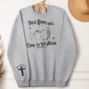 May include: Gray sweatshirt with a graphic of two skeletons dancing with stars and the text "These bones will come to life again Ezekiel 37:4-5".