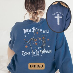 May include: Indigo blue sweatshirt with a graphic of two skeletons dancing with stars and the text "These bones will come to life again Ezekiel 37:4-5". The back of the sweatshirt has a white cross with the text "Ezekiel 37:4-5".