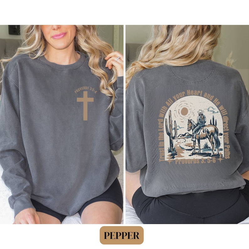 May include: A gray sweatshirt with a cross and the text "Proverbs 3:5-6" on the front. The back of the sweatshirt features a cowboy riding a horse in a desert landscape with the text "Trust in the Lord with all your heart and He will direct your paths" and "Proverbs 3:5-6".
