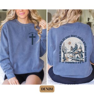 May include: A blue denim sweatshirt with a cross on the front and a cowboy riding a horse with the text "Trust in the Lord with All your Heart and He will direct your Paths" and "Proverbs 3:5-6" on the back.