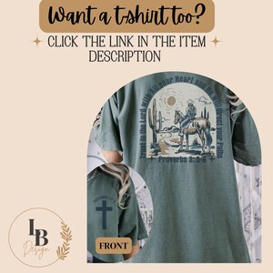 May include: A green t-shirt with a graphic print of a woman riding a horse in a desert landscape. The text "Trust in the Lord with all your Heart and He will direct your Paths" is printed around the graphic. The text "Proverbs 3:5-6" is printed below the graphic. The front of the shirt has a cross graphic and the text "Proverbs 3:5-6".