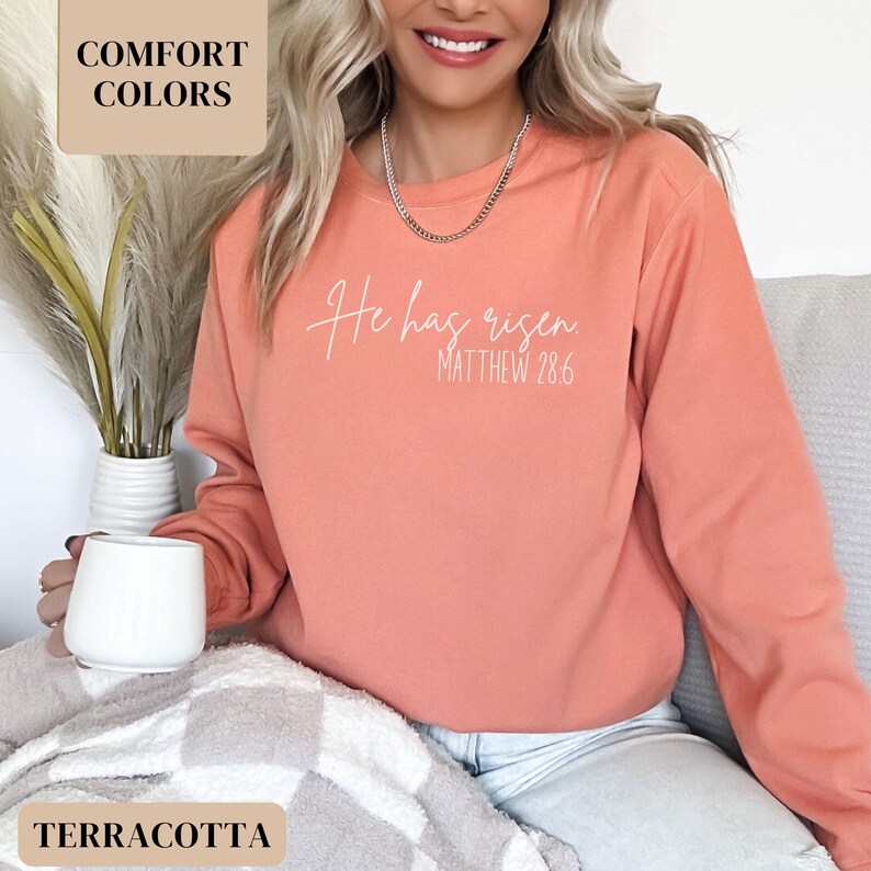 May include: A terracotta colored sweatshirt with the text "He has risen. Matthew 28:6" in white.