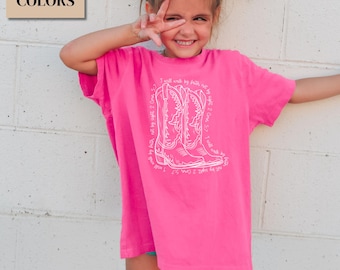May include: A bright pink t-shirt with a white graphic of cowboy boots and the text "I will walk by faith, not by sight 2 Cor. 5:7". The shirt is labeled "Comfort Colors" and "Crunchberry".