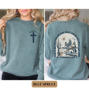 May include: A blue sweatshirt with a cross and the text "Proverbs 3:5-6" on the front. The back of the sweatshirt features a cowboy riding a horse in a desert landscape with the text "Trust in the Lord with All your Heart and He will direct your Paths" and "Proverbs 3:5-6".